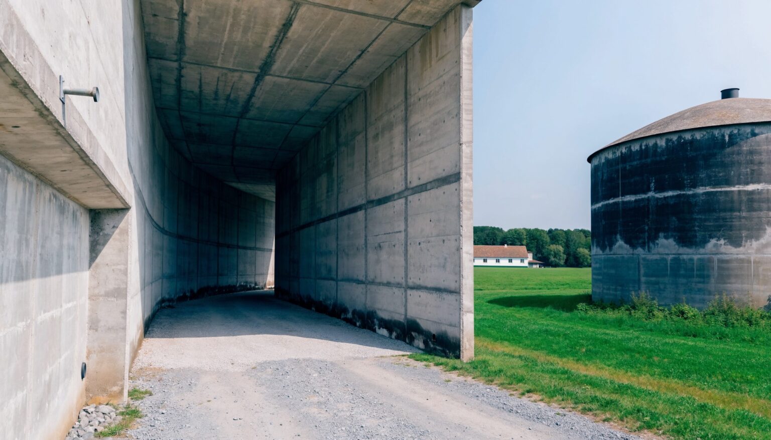 Fahrsilo mit hohen Sichtbeton-Wänden und runder Beton-Güllebehälter auf einem Bauernhof, grüne Wiese im Hintergrund