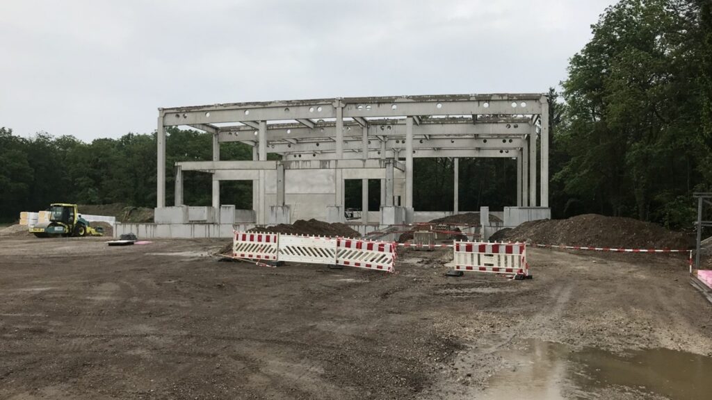 Rohbau einer Halle aus Betonfertigteilen mit Stützen und Bindern auf der Baustelle – Maschinenhalle errichten mit Fundamenten, Bodenplatte und Fertigteilwänden